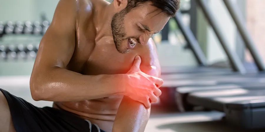 Homem em treino de musculação segurando o ombro com dor
